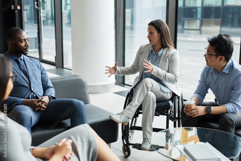 Wall mural diverse group of business people meeting in office lobby with focus on young woman in wheelchair sha