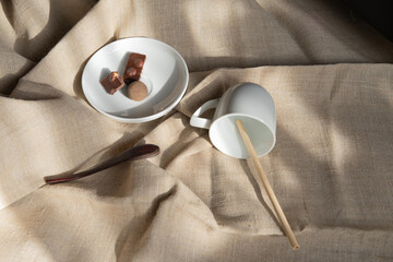White saucer with chopped chocolate and round candy truffle next to a wooden teaspoon and empty cup...