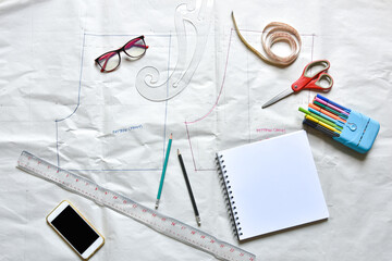 Sewing supplies on a draft paper of pants, sewing thread, scissors, , colorful pen, pencil, ruler, sketch book, smartphone ,centimeter tape and equipment