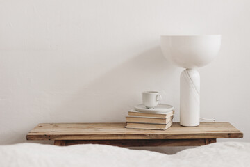 Cup of coffee on pile of books and modern marble geometric lamp. Vintage bench, table. White wall...