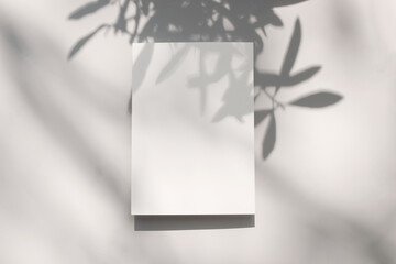 Summer stationery mock-up scene. Blank vertical greeting card with olive tree leaf and branches shadow overlay. Baige table background in sunlight. Flat lay, top view. Modern Mediterranean design.