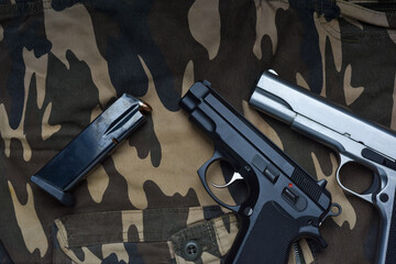 Still life with black and silver handgun with cartridge magazine on camouflage soldier pant...