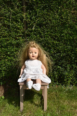 High angle of a creepy old doll with disheveled hair sitting in the garden