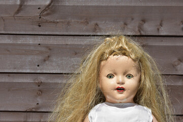 Closeup of a creepy old doll with disheveled hair on wooden background