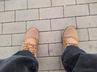 legs in brown boots on the sidewalk in the park first person view