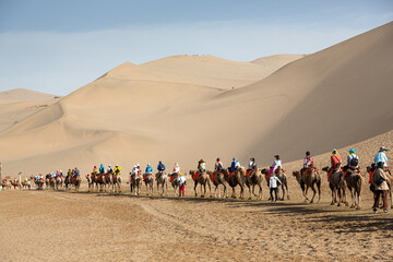 Touristen reiten auf Kamelen durch die Sanddünen bei Dunhuang in China.