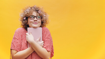 Naklejka premium Excited young woman student or writer holding book and thinking. Curly hair full of spring flowers. High quality photo