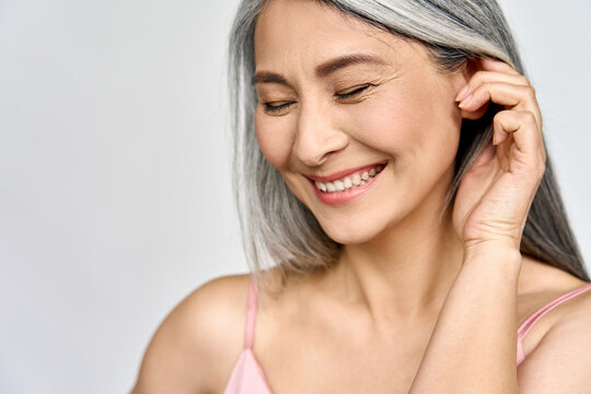 Portrait of gorgeous happy middle aged mature cheerful asian woman, senior older 50s lady pampering her face eyes closed isolated on white. Ads of lifting anti wrinkle skin care, spa. Copy space.