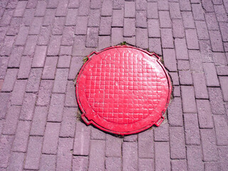 Red sewer manhole on lilac paving slabs close-up, top view.