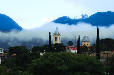 Large image of a beautiful misty mountain landscape in a small town called Joanopolis in the countryside of Brazil. Catholic church clock and bell tower view among foggy mountains and stunning nature