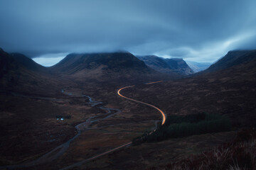 Morning landscape with car lights on the mountain road leading to Glencoe opposite Buachaille Etive Mor. A82 road before dawn. Scotland