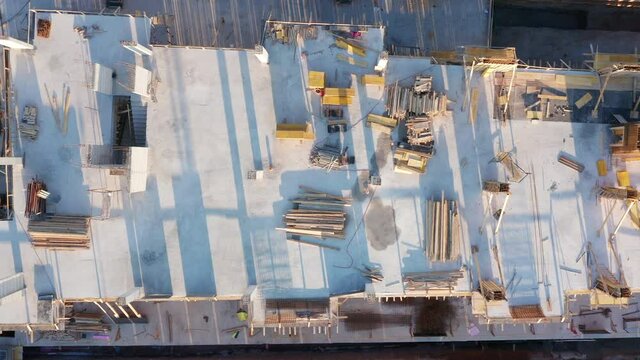 Construction site of a building made of reinforced concrete. Slab and columns as parts of the frame, with steel bars (rebars), mesh and formwork timber scattered around. Aerial drone top down view.