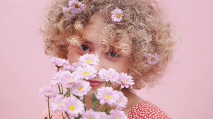 Naklejka premium Happy young woman smelling bouquet of spring roses. Portrait of caucasian girl with flowers in her curly hair . High quality photo