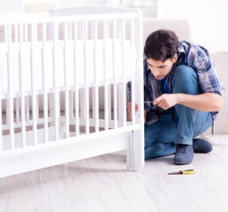 Young man assembling baby bed with instruction manual