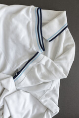 white polo shirt with light and dark blue piping on dark grey - photographed from above with low or raking light - emphasis on texture and folds