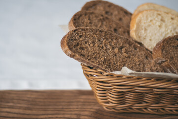 Partially blurred wicker basket with black and white bread on white tablecloth on wooden table