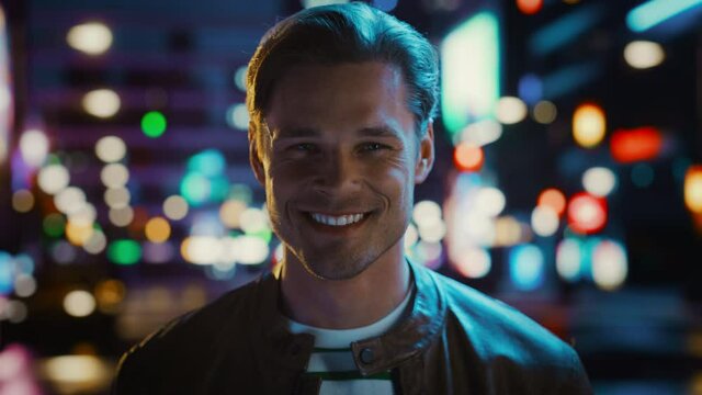 Portrait of Handsome Blonde Man Smiling, Looking at Camera, Standing in Night City with Bokeh Neon Street Lights in Background. Happy Confident Young Man with Stylish Hair. Closeup Tilting Shot