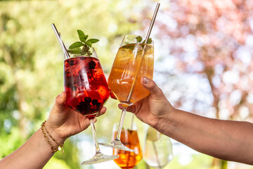 Clinking glasses with refreshing summer cocktails, two people holding glasses with colorful...