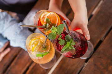 Close-up of three persons clinking glasses with colorful fresh and tasty summer cocktails, friends...