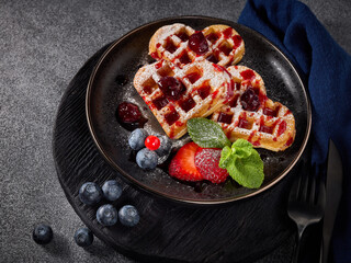 Delicious waffles heart shape with  powdered sugar and berries on  plate on grey background. Sweet meal. Dessert