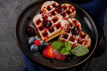 Delicious waffles heart shape with  powdered sugar and berries on  plate on grey background. Top view.  Sweet meal. Dessert