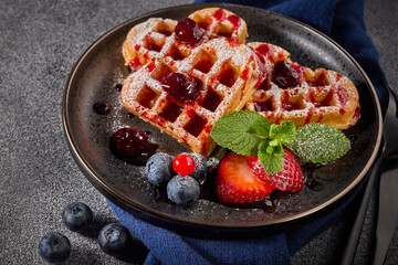 Delicious waffles heart shape with  powdered sugar and berries on  plate on grey background. Top view.  Sweet meal. Dessert