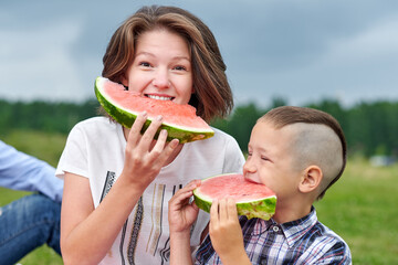 Mother and son eating watermelon in meadow or park. Happy family on picnic. outdoor portrait Little boy and mom