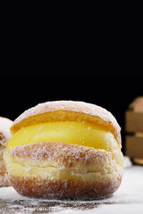 Berlin balls, known as Sonho in Brazil on wooden table with scattered icing sugar. It consists of a fried sweet dough filled with a cream and sugar on top. Selective focus. Vertical.
