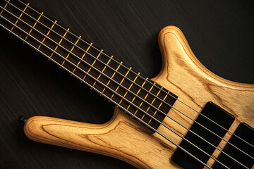 Fototapeta na wymiar Close up of electric bass guitar with five strings. Detailed view of wooden varnished texture of musical instrument on dark brown background. Music classes, concert, hobby and bass player concept 