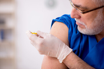 Old male doctor in vaccination concept