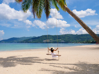 Phuket, Thailand. Tropical beach paradise with beach swing with girl in white shirt. Women relax on swing under coconut palm tree at beautiful tropical beach White sand. vacation summer holiday