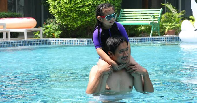 Asian father with little daughter piggyback in swimmingpool at park. Family Leisure and travel at holidays.