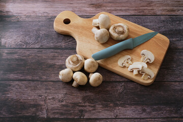 Top view of fresh Agaricus bisporus or .Champignon mushroom with knife on wooden cutting board on wooden background.