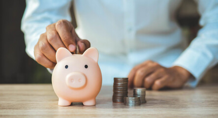 Saving money wealth and financial concept.piggy bank with coin on old wooden table.Financial planning.man's hand putting money into piggy bank.