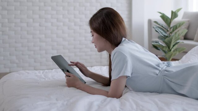Asian woman paying online. Shopper shopping online and taplet on bed.