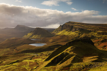 Naklejka na ściany i meble Scenic view of Quiraing mountains in Isle of Skye, Scottish highlands, United Kingdom. Sunrise time with colourful an rayini clouds in background.