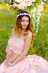 Fototapeta na wymiar Young happy pregnant woman relaxing and enjoying life in nature. Beautiful portrait of a pregnant woman on a warm summer day in the garden. Attractive pregnant woman relaxing outside. Future mom