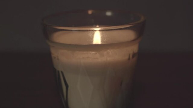Close macro view of glass white wax candle and bright yellow flame at home. Decoration object