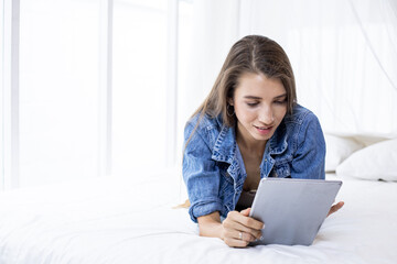 Young woman playing tablet on the bed.