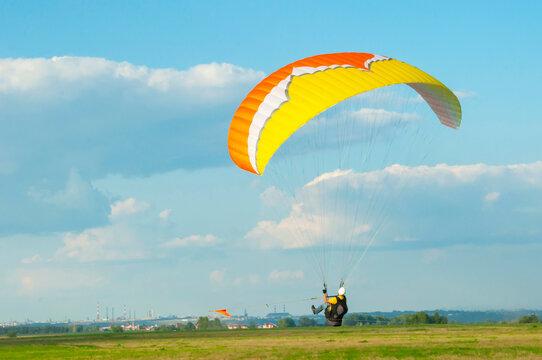 paraglider with a man in the sky on the background of a city landscape with factories and a blue sky with cloud