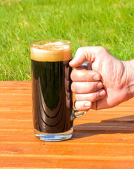 a cup of dark beer on a orange table on a natural green background, pinta of black stout close up, glass of ale