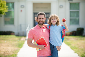 Portrait of teacher and happy pupil. Parent and pupil of primary school go hand in hand. Teacher in t-shirt and cute schoolboy with backpack near school park.