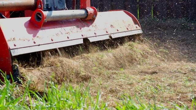 a tractor with a mower attached mulches dry grass along the fence. Land plot processing