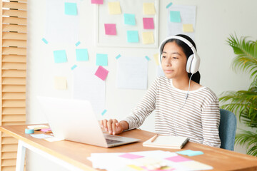 Happy Asian girl video call online via internet tutor on a computer laptop with headphone