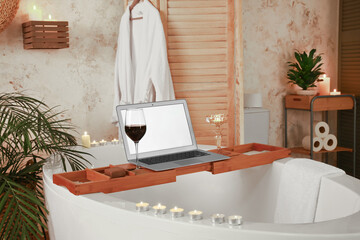 Stylish interior of modern bathroom with laptop and burning candles