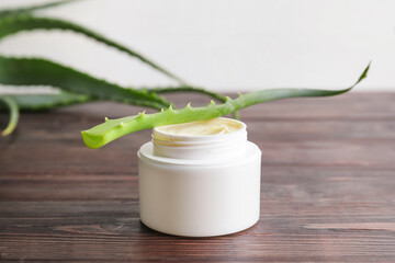 Jar with natural cream and aloe leaf on wooden background