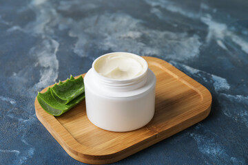 Jar with natural cream and aloe leaves on color background