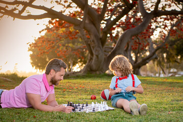 Happy family outdoor. Father and son playing chess in autumn garden.