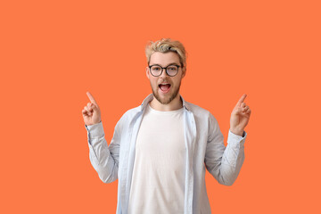 Young man wearing eyeglasses and pointing at something on color background