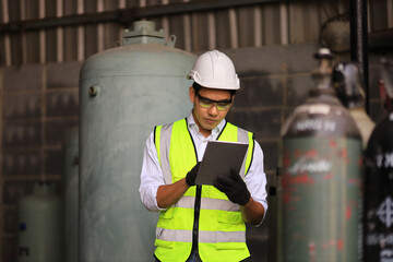 Asian industrial worker using digital tablet to check the coolant system in the factory while standing before liquid nitrogen and argon in compressed container tank for biochemical industry - obrazy, fototapety, plakaty